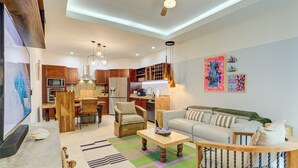 Un salon moderne avec un canapé, une table basse et un téléviseur. Il y a également un coin cuisine équipé de placards et d’appareils électroménagers.