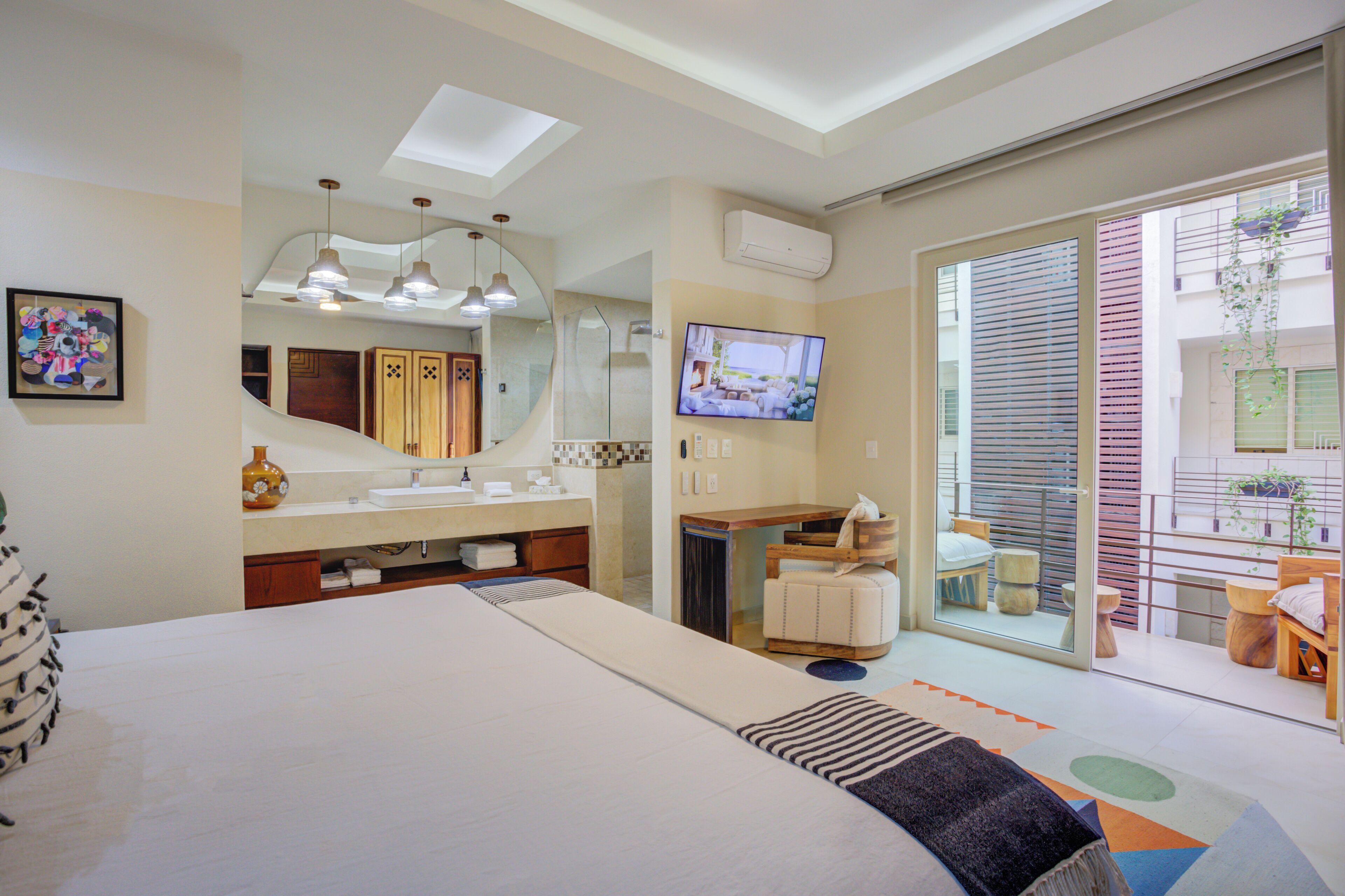 Une chambre d’hôtel moderne dotée d’un grand lit, d’une salle de bain avec un meuble-lavabo, d’une télévision et d’un balcon agrémenté de plantes.