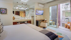 Une chambre d’hôtel moderne dotée d’un grand lit, d’une salle de bain avec un meuble-lavabo, d’une télévision et d’un balcon agrémenté de plantes.