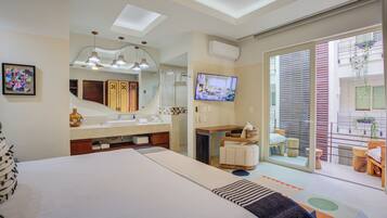 Una habitación de hotel moderna con una cama grande, un baño con tocador, una televisión y un balcón con plantas.