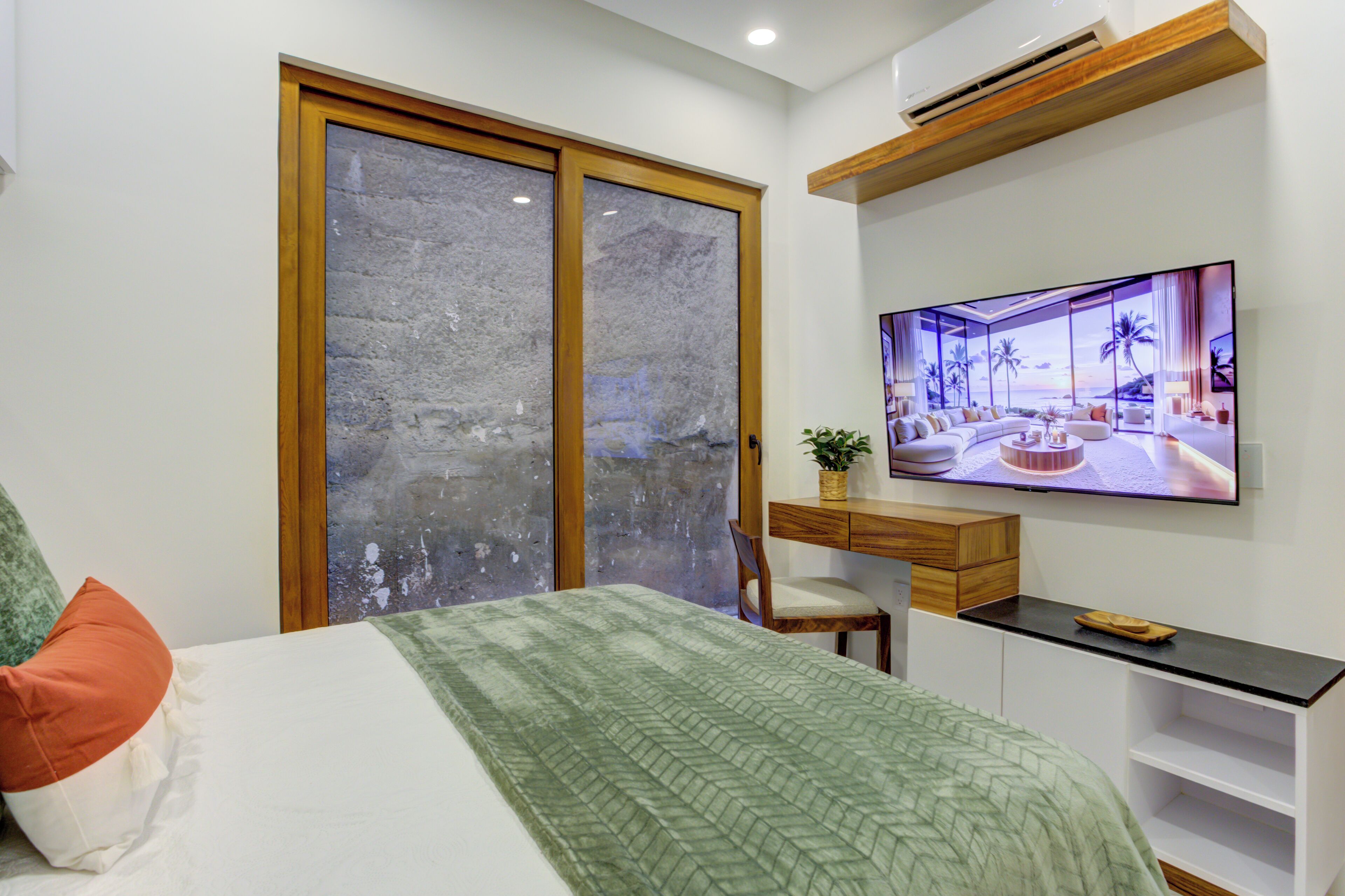 Un dormitorio con cama, escritorio, silla y televisor en la pared.