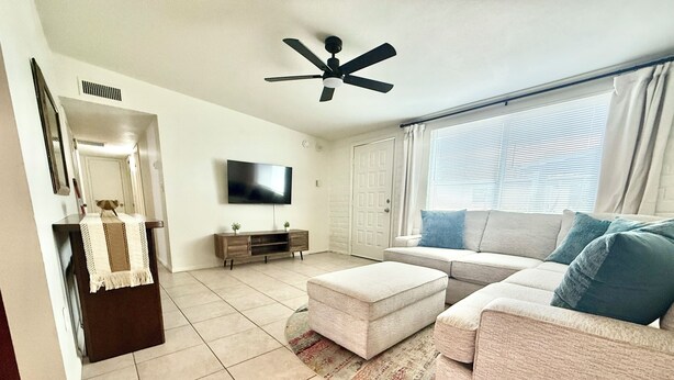 A living room with a ceiling fan, a flat-screen TV, a sofa, and a coffee table. - Bright and Cozy Tucson Condo - Ideal for families, couples and friends (Tucson)