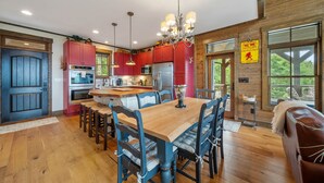 A spacious kitchen with red cabinets, a wooden dining table, and a chandelier. - Mountaintop Lodge with Views (Boone)