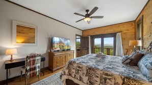 A bedroom with a bed, a desk, a chair, a television, and a view of the outdoors. - Mountaintop Lodge with Views (Boone)