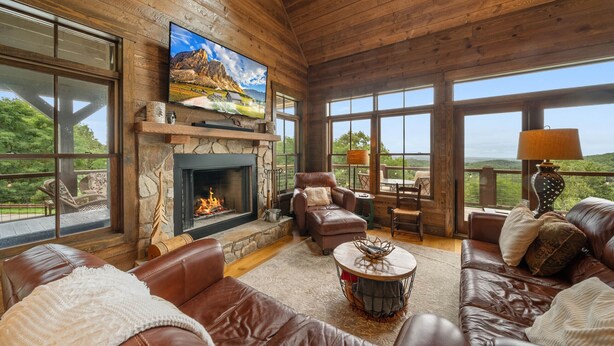 A spacious living room with a fireplace, leather sofas, a television, and large windows offering a view of the outdoors. - Mountaintop Lodge with Views (Boone)