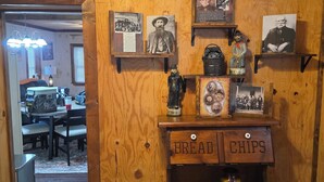 A wooden interior with a vintage-themed decor, including a wall-mounted shelf with historical photos and artifacts, a bread and chips cabinet, and a dining area with a table and chairs. - Rowdy Ridge Yee Yee (Northfork)