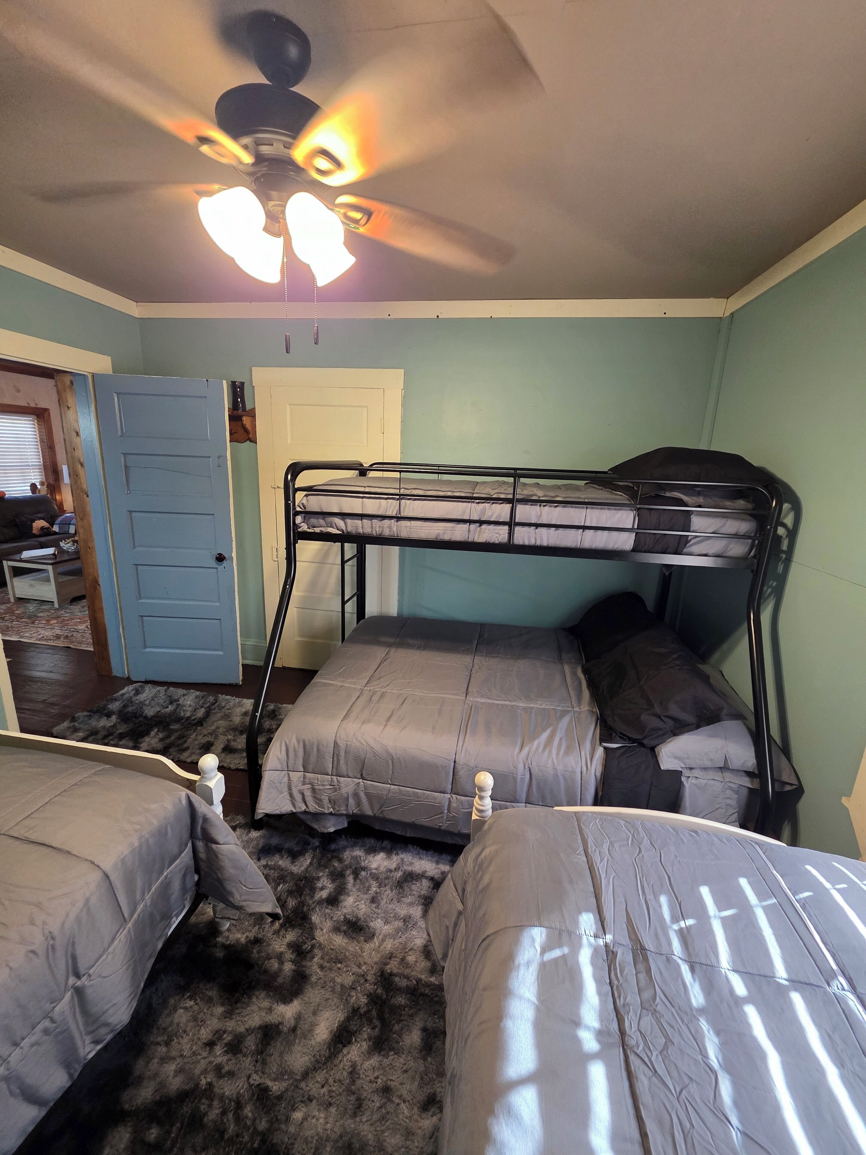 A room with a bunk bed, a ceiling fan, and a door leading to another room.