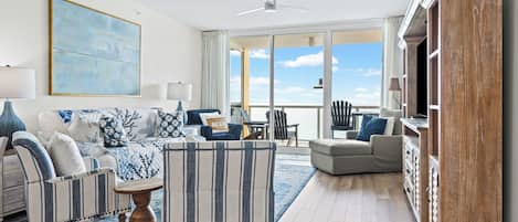 A spacious living room with a large window, a ceiling fan, and a view of the ocean.