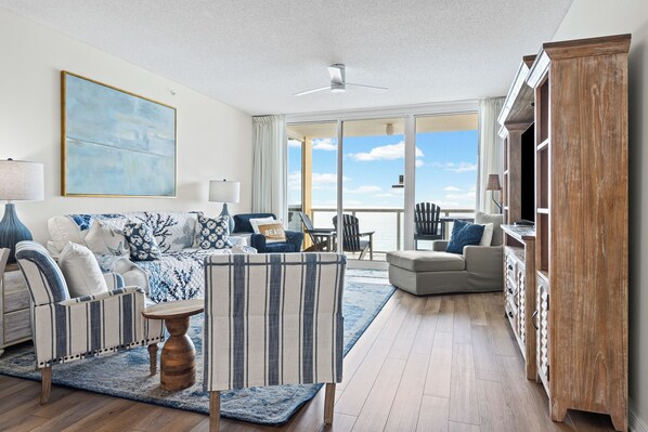 A spacious living room with a large window, a ceiling fan, and a view of the ocean.