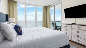 Quarto de hotel com uma cama grande, televisão, cômoda e varanda com vista para o oceano.