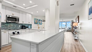 Cozinha moderna com armários brancos, uma ilha grande e vista para a sala de estar.