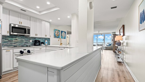 A modern kitchen with white cabinetry, a large island, and a view to the living area.