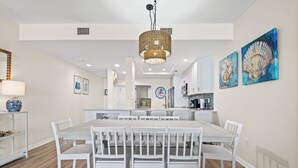 A modern kitchen with white cabinetry, a central island, and a dining area with white chairs.