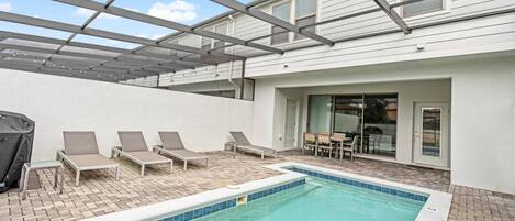 Un área de piscina en la azotea con sillones de descanso y un patio cubierto.