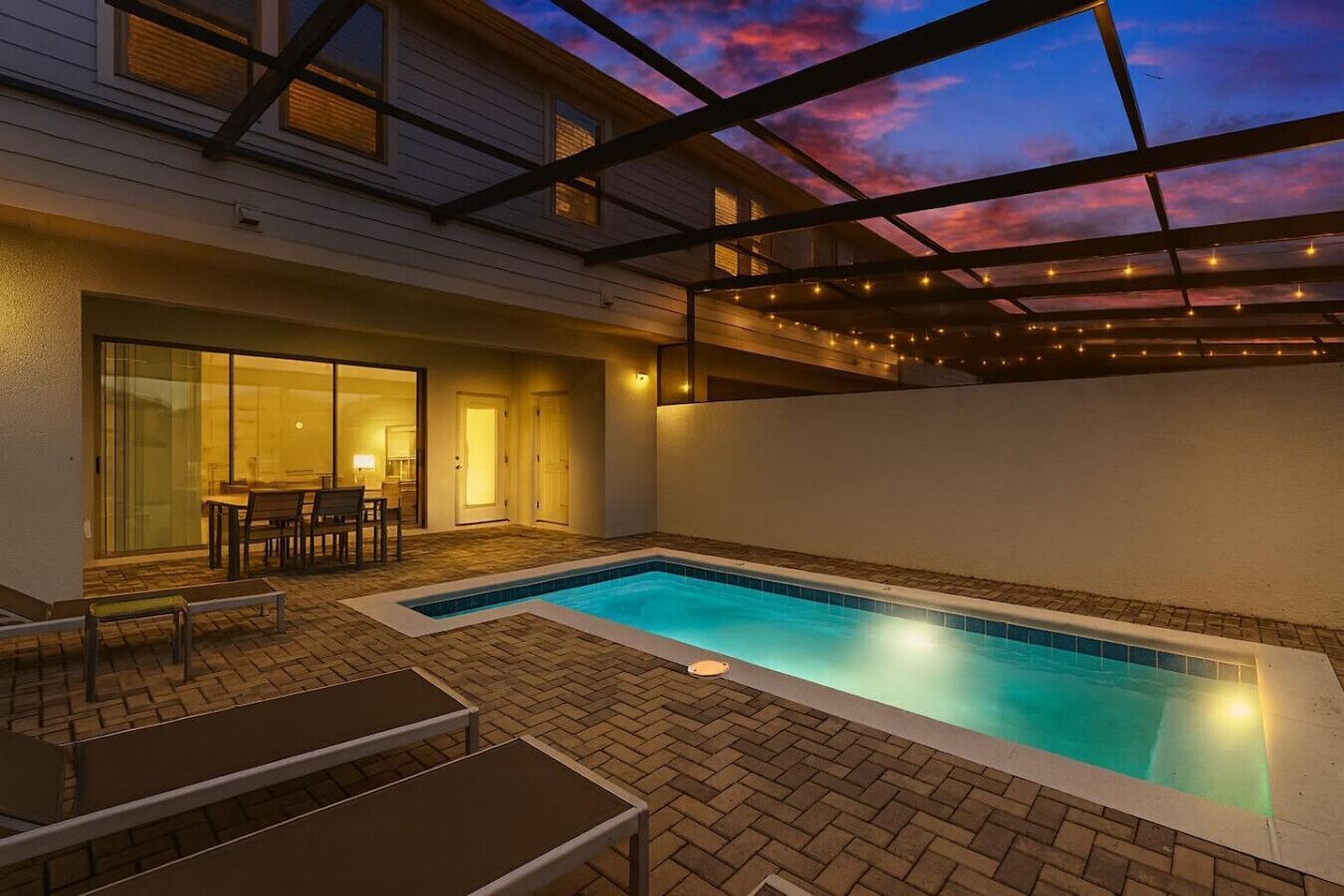 An outdoor swimming pool with a covered patio area, a dining table, and chairs.