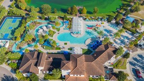 Vue aérienne d’un complexe hôtelier comprenant une piscine centrale, un court de tennis et plusieurs villas.
