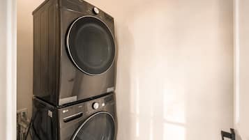 A stacked washer and dryer unit in a room with white walls and a door.