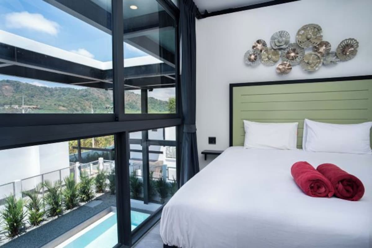 A hotel room with a large bed, a view of the outdoors, and a decorative wall piece.