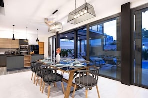 A modern kitchen with dark cabinets, a built-in oven, and a dining area with a wooden table and chairs. - Sunset Garden V1 (Phuket)