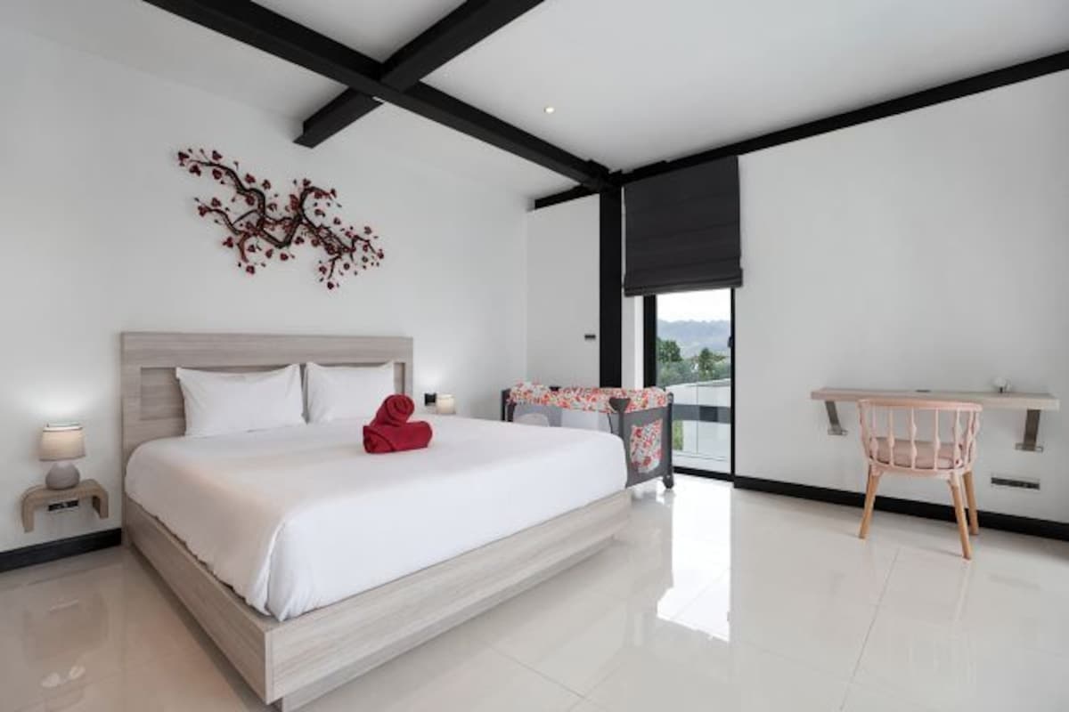 A modern bedroom with a large bed, a desk, and a balcony with a view.