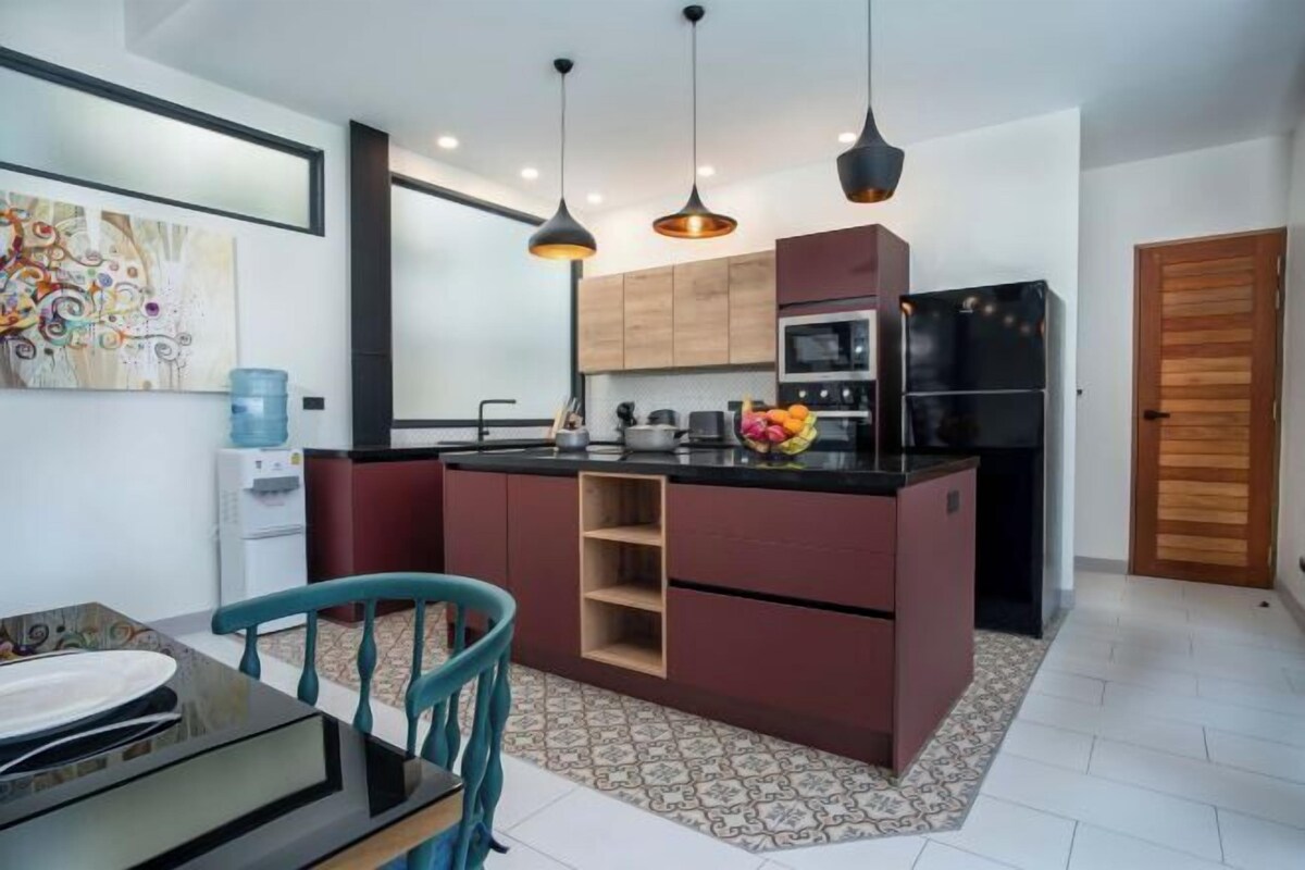 A modern kitchen with a central island, pendant lighting, and a dining area with a table and chairs.