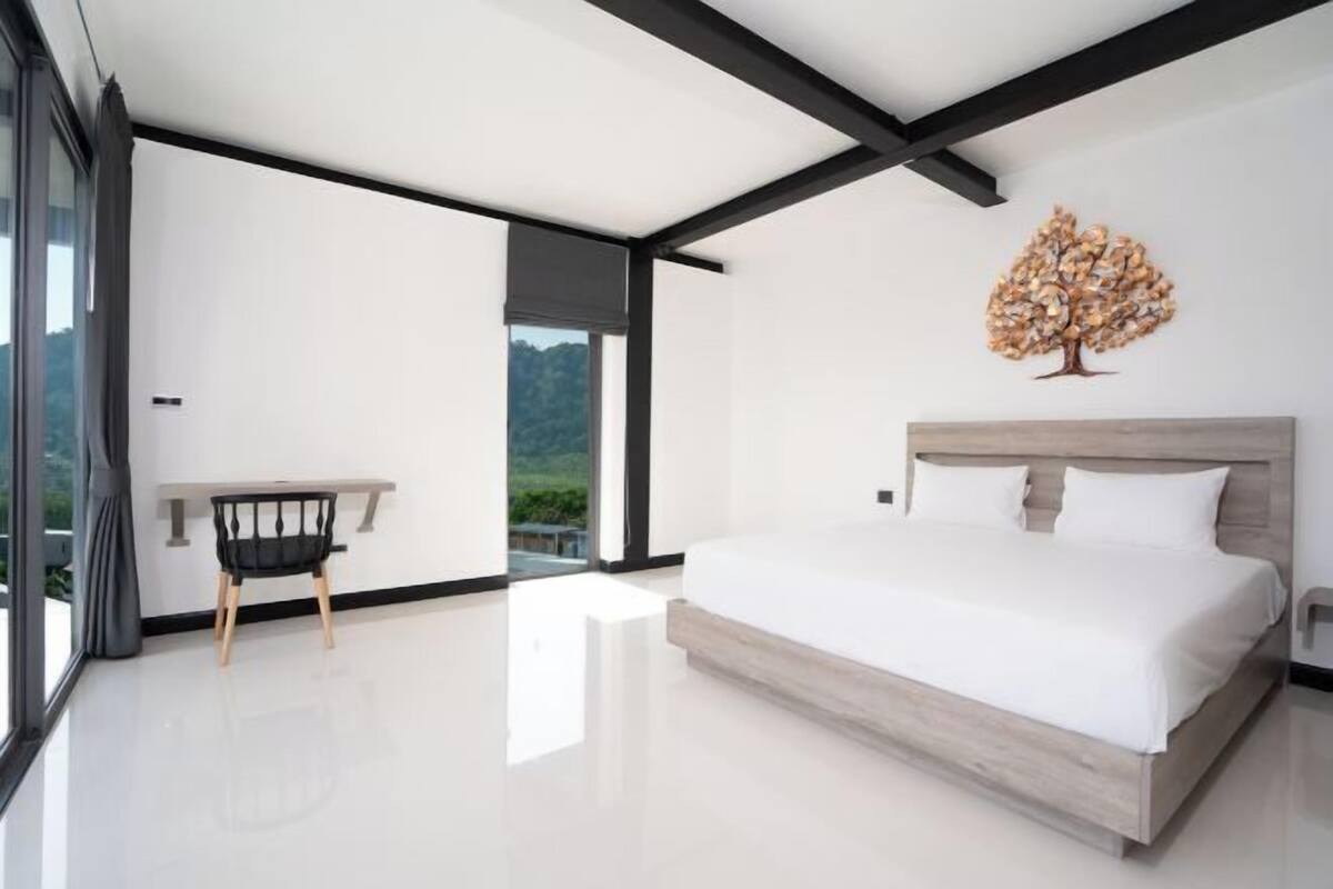 A modern bedroom with a large bed, a desk, and a view of the outdoors.
