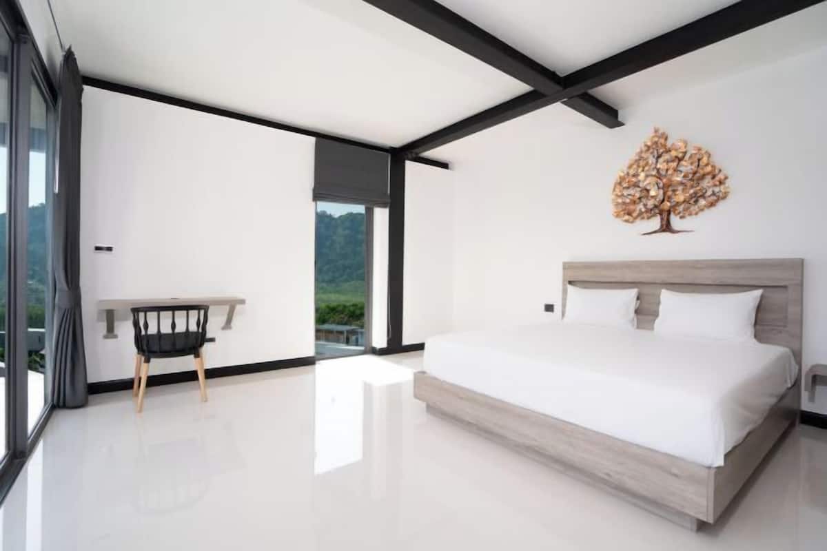 A modern bedroom with a large bed, a desk, and a view of the outdoors.