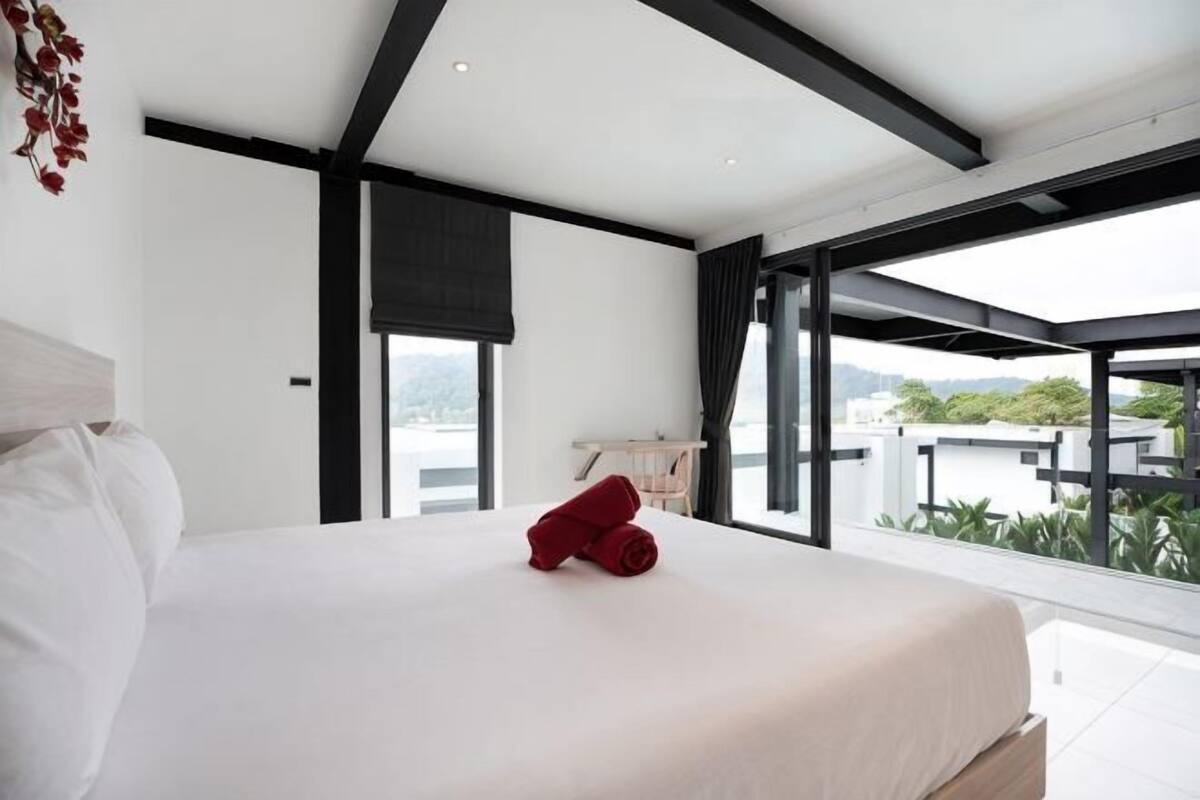 A modern bedroom with a large bed, a view of the outdoors, and a balcony.