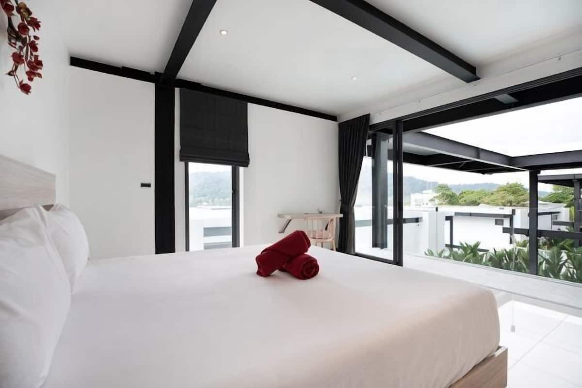 A modern bedroom with a large bed, a view of the outdoors, and a balcony.