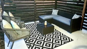 Uma área externa com espaço para sentar, incluindo um sofá, poltrona e mesa de centro, cercada por um cercado de madeira.