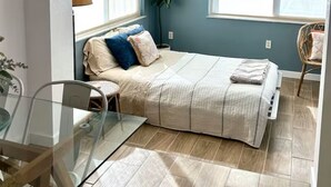 Quarto com cama, ventoinha no teto, janela, planta e cadeira.