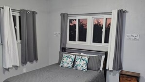 Ein Schlafzimmer mit Bett, Nachttisch, Fenster und Deckenventilator.