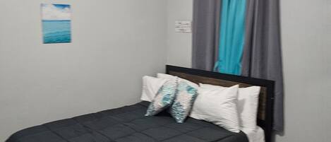 A bedroom with a bed, a bench, an air conditioning unit, and a window with curtains.