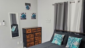 A modern bedroom with a large bed, a dresser, a mirror, and artwork on the wall.