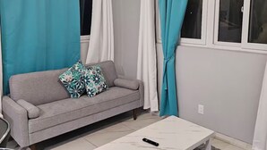 A modern living room with a grey sofa, teal curtains, a white coffee table, and a grey rug.