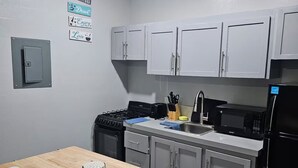 A kitchen with white cabinets, a stove, a sink, and a refrigerator. There are signs on the wall and a table with a roll of paper towels.