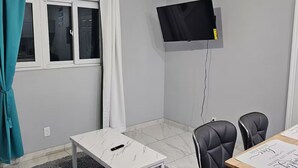 A modern room with a ceiling fan, a flat-screen TV mounted on the wall, a small white table, two black chairs, and a grey rug.