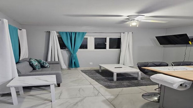 A modern living room with a sofa, a coffee table, a dining table, and a ceiling fan.