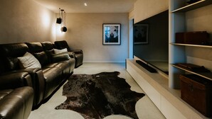 A modern living room with a leather sofa, a fur rug, and a flat-screen TV mounted on the wall. - Riverslea - Pool - Sleeps 10 (Wānaka)