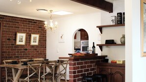 Un comedor con pared de ladrillo, sillas de madera, una araña y una cocina al fondo.