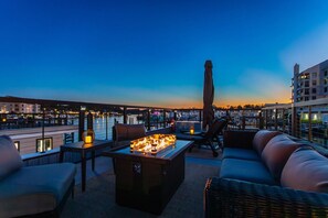 Eine Dachterrasse mit Feuerstelle, Sitzgelegenheiten und Blick auf die Stadt bei Dämmerung.