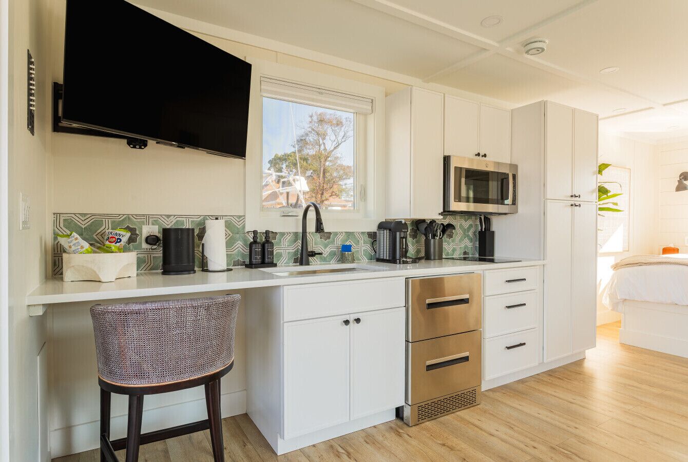 Una cocina moderna con armarios blancos, un microondas de acero inoxidable y un taburete de bar.
