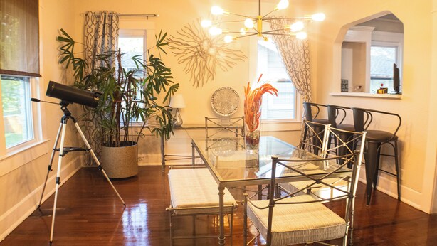 A dining area with a glass table surrounded by metal chairs, a tripod stand, and potted plants.
