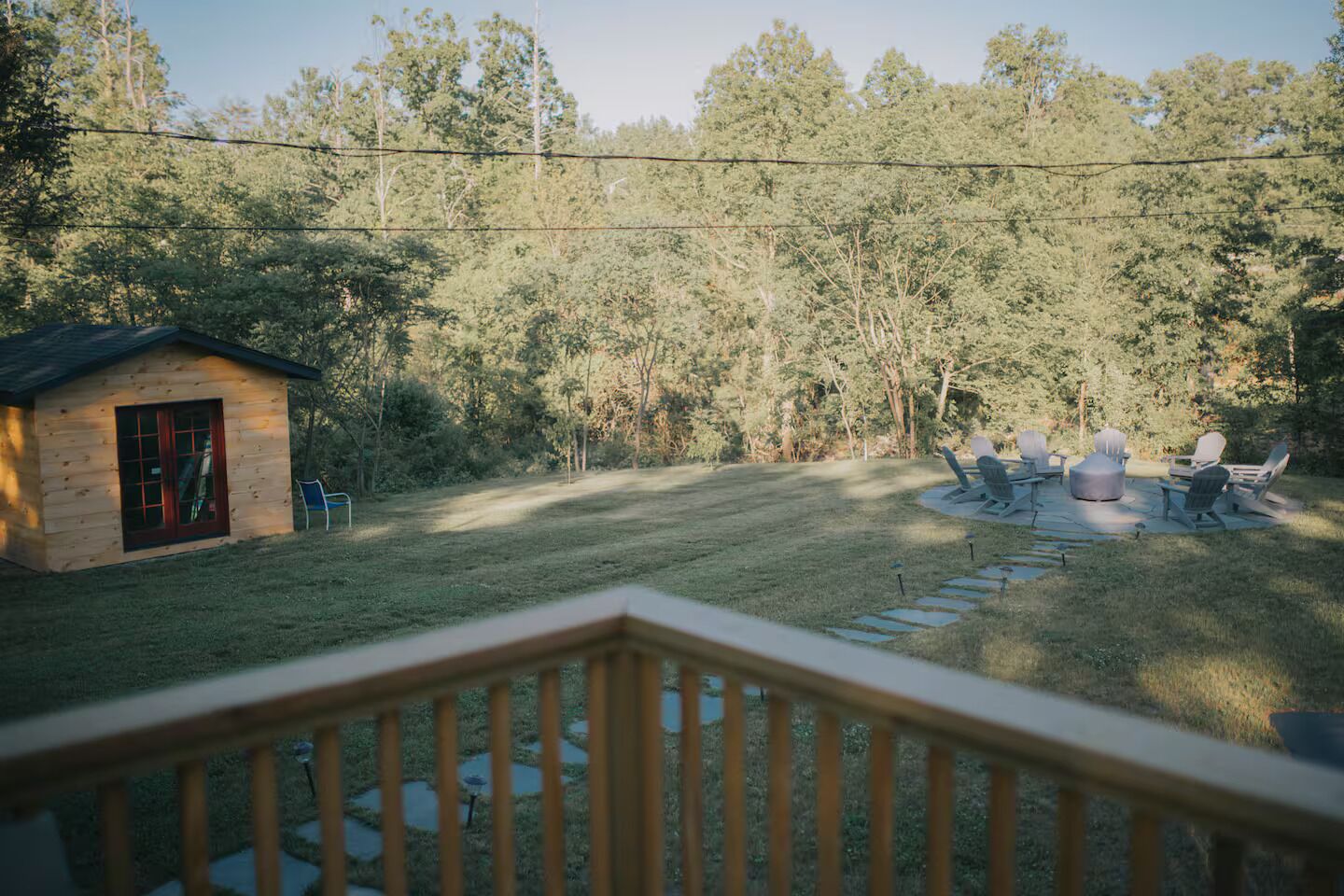 A wooden cabin with a red door, a small porch, and a deck overlooking a grassy yard with a fire pit and outdoor seating.