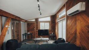 Uma sala de estar aconchegante com uma televisão grande, paredes de madeira e uma luminária no teto.