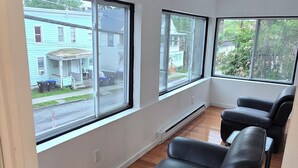 A room with large windows, a black leather sofa, and wooden flooring. - Stunning 5-bedroom house with AC / Heat in charming Poughkeepsie NY (Poughkeepsie)