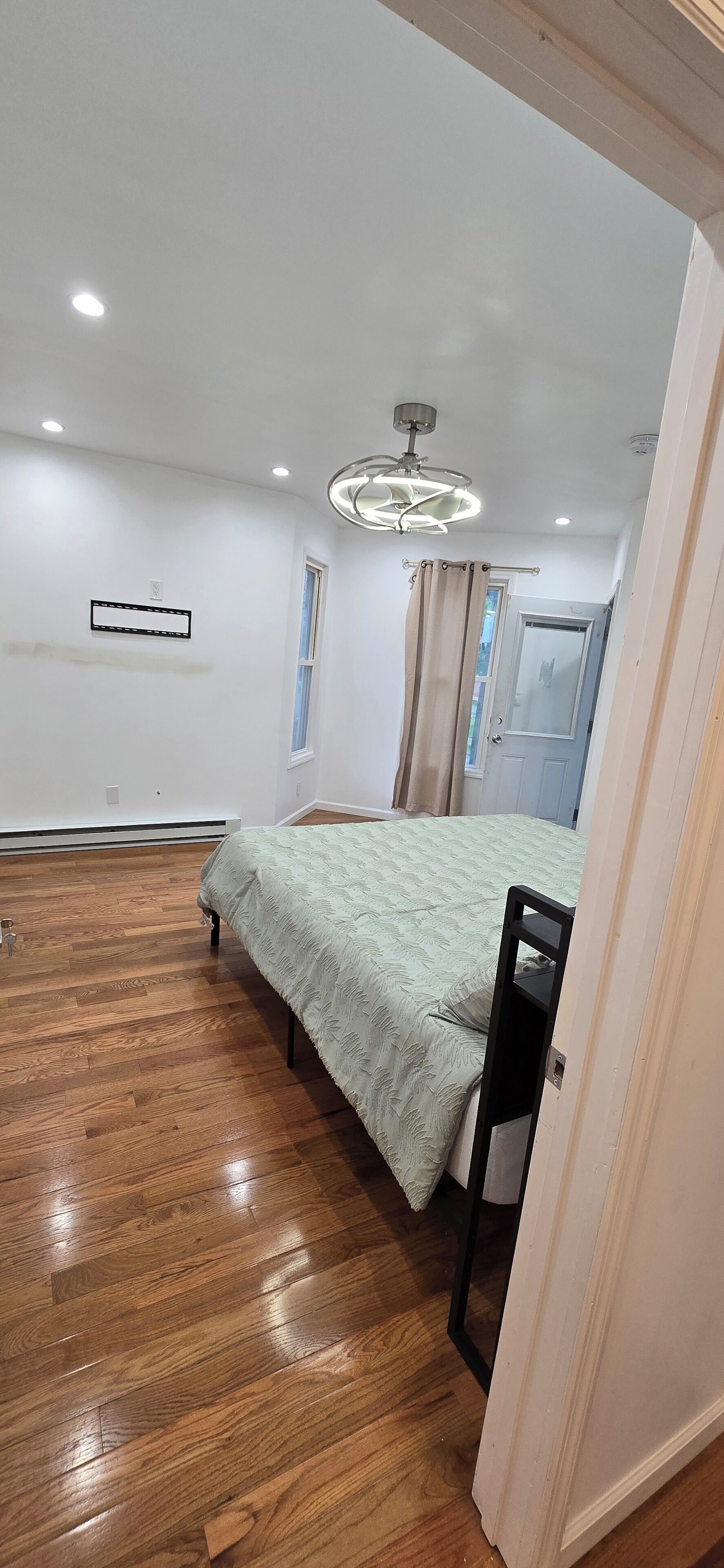 Una camera da letto con un letto, pavimento in legno, un lampadario a soffitto, una finestra e una porta.