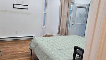 Un dormitorio con cama, suelo de madera, lámpara de techo, ventana y puerta.