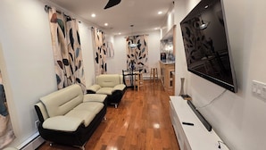 A modern living room with a sofa, a TV, and a dining area with a table and chairs. - Stunning 5-bedroom house with AC / Heat in charming Poughkeepsie NY (Poughkeepsie)