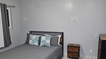 A bedroom with a bed, a nightstand, a dresser, a ceiling fan, and two wall decorations.